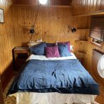 Image de la cabine située à droite du bateau. Elle est composée d'un lit double situé au centre de la pièce. La parure de lit est bleue, blanche et violette.