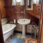 Image de la salle de bain privative de la cabine arrière. Elle comprend une baignoire à gauche, un lavabo au centre et un toilette avec une cuvette en bois à droite.