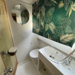 Photo de la salle de bain attenante à la troisième cabine du bateau. Elle est blanche avec, comme pour l'autre salle de bain, un toilette, un évier ainsi qu'un store aux motifs tropicaux installé au-dessus de l'évier.