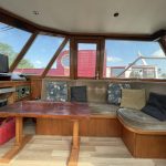 Image de la banquette du bateau. Une table rectangulaire en bois de couleur bordeaux se situ devant elle. A gauche, une télévision.