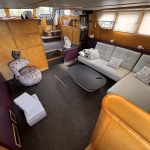 Photo du salon située à l'entrée du bateau. On y voit un canapé d'angle blanc, une table basse noire et des meubles de rangement en bois