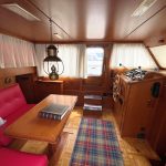 Vue depuis la porte d'entrée du bateau. On voit à gauche une banquette rouge avec des coussins à carreaux. A droite, le poste de pilotage.