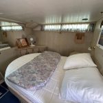 Autre vue de la cabine arrière . On voit un meuble de rangement en bois beige clair avec un ventilateur placé dessus. Un miroir prenant l'ensemble du mur se trouve en face du lit.