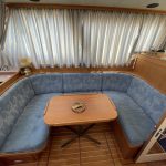 Photo de la banquette avec une table rectangulaire à bords ronds en son centre. Derrière, des rideaux à rayures blanches et bleu clair.