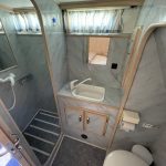Photo de la salle de bain en marbre blanc et gris. A gauche, la douche, au centre le lavabo et à droite les toilettes.