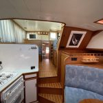Vue d'ensemble de l'intérieur du bateau depuis la cuisine. On y voit deux marches d'escalier en bois avec des rayures blanches permettant d'accéder à la pièce à vivre.